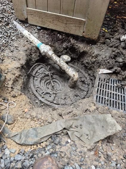 Exposed piping and drainage components are visible beside a gate during work.