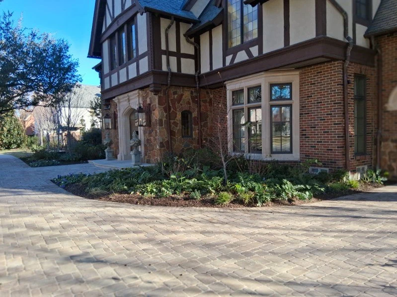 Layered foliage softens the edge of a broad paved residential entrance.