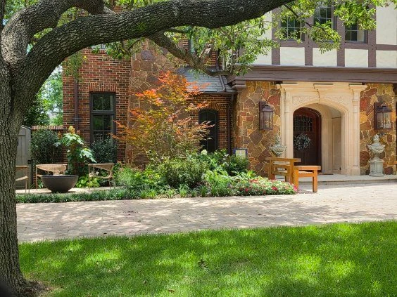 A mature tree frames lawn, garden seating, and planting near the front door.