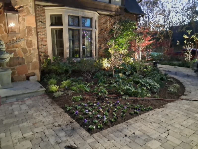 New flowers and mixed foliage fill a bed beside a stone-paved entrance.