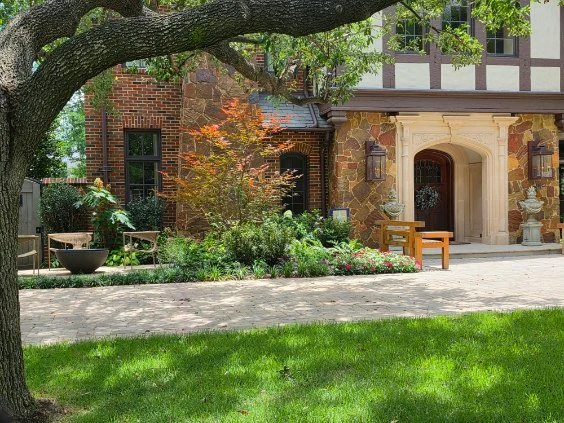 Lawn, ornamental planting, and garden seating frame the entrance to a home.