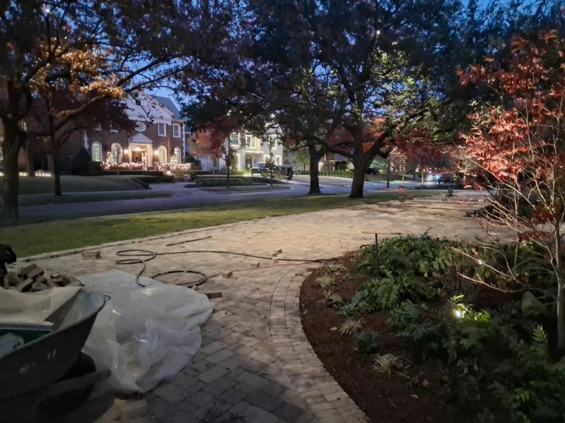 Tools and materials sit beside a paved driveway during an evening landscape project.