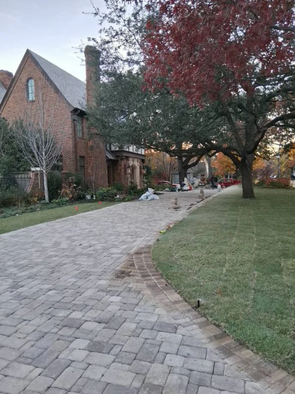A curved paved driveway borders lawn and planting while landscape work is underway.