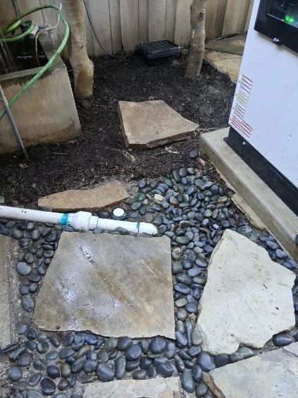 Stepping stones and river rock define the ground around outdoor utility piping.