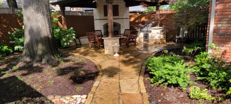 A stone path winds between planted beds toward a covered outdoor seating area.