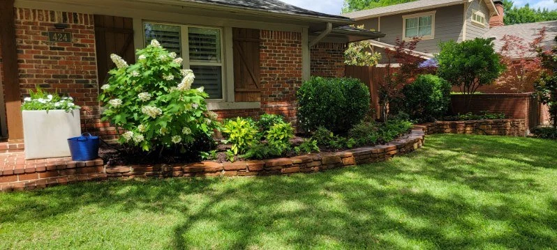 Layered shrubs and flowering plants follow a curved stacked-stone border.