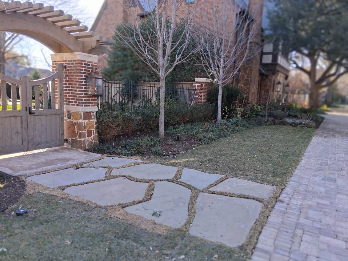 Large stepping stones lead toward a gate beside lawn and planted borders.