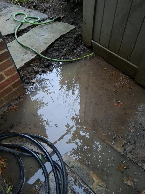 Water collects beside a gate and stepping stones in this drainage work-area photo.